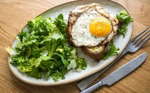 Ein Croque Madame mit Spiegelei, Käse und Toast, serviert mit frischem Salat.
