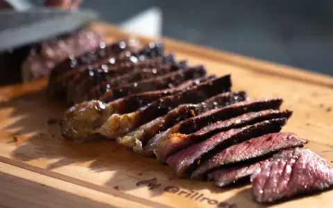 Saftiges Steak, auf einer Plancha zubereitet, wird auf einem Holzbrett in Scheiben geschnitten.