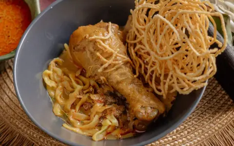 Khao Soi: Hühnerkeule in cremiger Kokosmilch-Currysauce mit weichen und knusprigen Nudeln.
