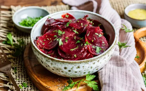 Schüssel mit traditionellem Rote Bete Salat, garniert mit Petersilie. Daneben kleine Schälchen mit Kräutern und Dressing.