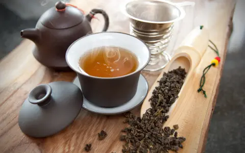Dampf steigt aus einer Tasse Oolong Tee auf. Daneben liegen lose Teeblätter in einer Holzschaufel. So schmeckt Oolong Tee: mild, blumig, leicht süßlich.