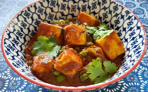 Schüssel mit cremigem Mattar Paneer, garniert mit Koriander. Die Sauce ist reichhaltig und rotbraun, mit Erbsen und würzigen Paneer-Würfeln.