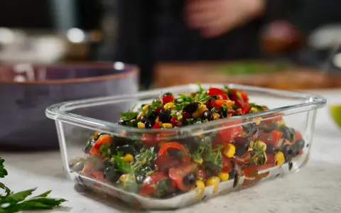 Frischer schwarze bohnen salat mit Mais, Tomaten und Kräutern in einer Glasbox, bereit zum Mitnehmen.