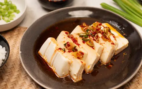 Seidiger Tofu, ein einfaches silken tofu recipe, serviert mit Frühlingszwiebeln und Chili-Öl auf einem dunklen Teller.