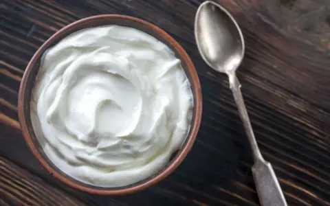 Schüssel mit cremiger Joghurt-Textur, eine tolle Alternative, wenn man fragt, was kann man statt Creme Fraiche nehmen. Daneben eine Löffel.
