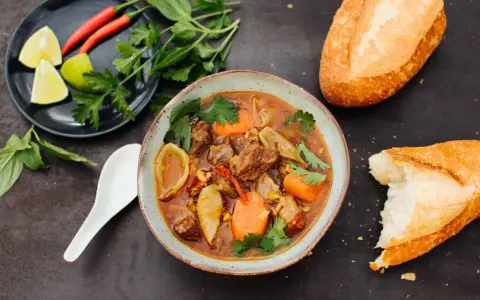 Herzhaftes Bo Kho, ein vietnamesischer Rindfleischeintopf mit Karotten und Kräutern, serviert mit Baguette.