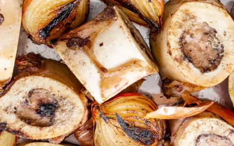 Rinderknochen auskochen Rezept: Geröstete Rinderknochen und Zwiebeln auf einem Blech, bereit für eine herzhafte Brühe.