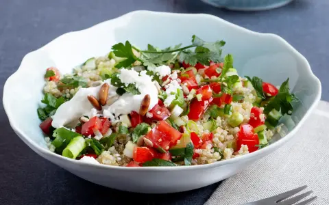 Frischer Quinoa-Salat mit Feta, Tomaten, Gurken und Kräutern, garniert mit Joghurt und Pinienkernen.
