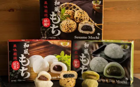 Verschiedene Sorten japanischer Reiskuchen (Mochi) mit Sesam, roter Bohne und grünem Tee, auf dunklem Untergrund vor Holz.