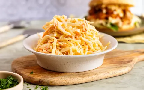 Schüssel mit cremigem Coleslaw, perfekt für das **rezept coleslaw original**. Im Hintergrund ein Burger.