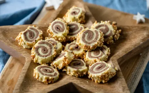 Haselnuss Kekse mit Schoko-Muster, umhüllt von gehackten Nüssen, auf einem Holzbrett.