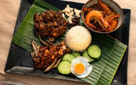 Nasi Lemak: Reis, scharfe Garnelen, frittierte Sardellen, Spiegelei, Gurkenscheiben, Cashewkerne und Rosinen auf Bananenblatt.