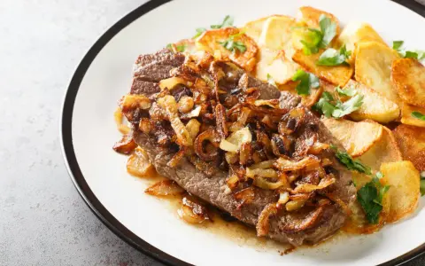 Ein saftiges Stück Rindfleisch, bedeckt mit goldbraunen Röstzwiebeln, serviert mit knusprigen Bratkartoffeln. Das ist der beste Zwiebelrostbraten!