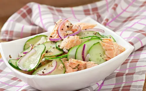 Frischer Gurkensalat mit zarten Lachsstücken und roten Zwiebelringen, gewürzt mit Pfeffer. Ein leichter und gesunder Salat.