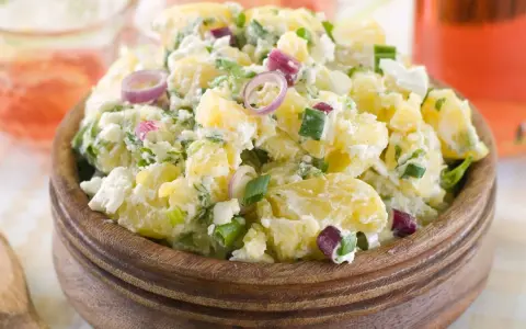 Herzhafter Kartoffelsalat mit Meerrettich, verfeinert mit Frühlingszwiebeln und roten Zwiebelringen, serviert in einer Holzschale.
