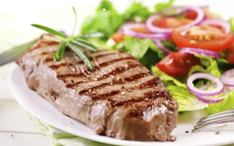 Ein saftiges Steak mit Grillstreifen, garniert mit Rosmarin, neben einem frischen Salat aus knackigem Grün, Tomaten und roten Zwiebelringen. Ein perfekter Steak Salat.