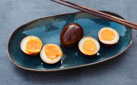 Dunkelbraune, marinierte Ramen-Eier auf einem blauen Teller, drei davon halbiert, mit flüssigem Eigelb.