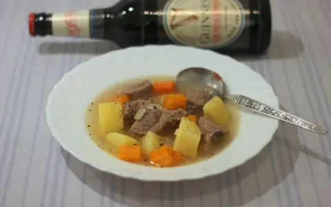Herzhafter Irish Stew mit Kartoffeln und Karotten in einer Schüssel, daneben eine Flasche Guinness.
