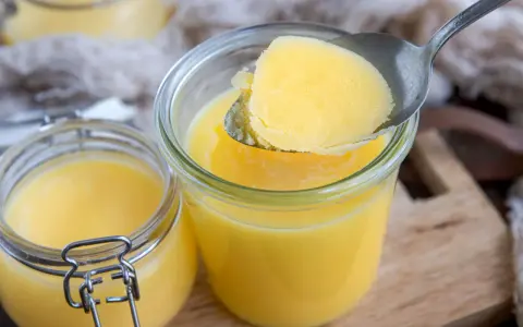 Ein Löffel Butterschmalz wird aus einem Glas gehoben. Dieses goldgelbe Fett ist ideal zum Braten, da sein hoher Butterschmalz rauchpunkt Verbrennungen verhindert.