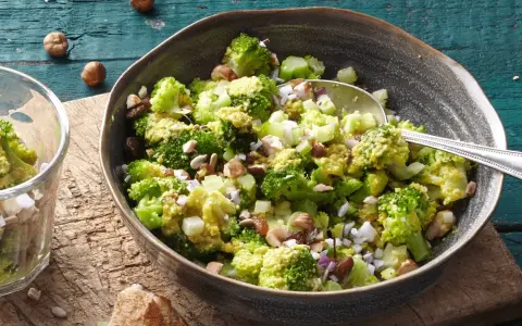 Ein einfacher Brokkoli-Salat mit Nüssen und Rosinen, serviert in einer Schüssel auf einem Holztisch.