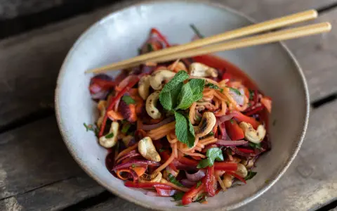 Bunter Papaya-Salat mit reifer Papaya, Karottenstreifen, Cashewkernen und Minze, serviert mit Stäbchen.