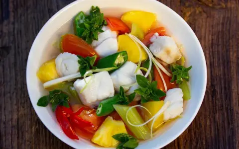 Ein Schüssel mit Canh Chua, einem vietnamesischen Fisch-Gemüse-Eintopf, mit Ananas, Tomaten, Okra und Kräutern.