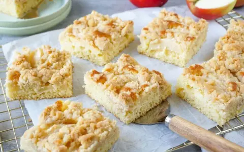 Saftige Stücke vom besten Apfelkuchen mit Streusel, frisch gebacken und bereit zum Genießen. Äpfel liegen daneben.