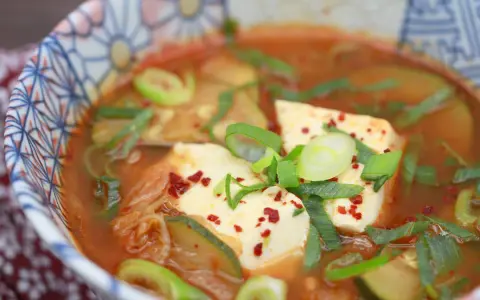 Heißes, würziges Sundubu Jjigae mit weichem Tofu, Kimchi und Frühlingszwiebeln in einer bunten Schüssel.
