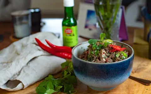 Würziges Laab Moo, ein thailändischer Hackfleischsalat, garniert mit frischer Minze und Chili. Daneben liegen rote Chilis und Koriander.