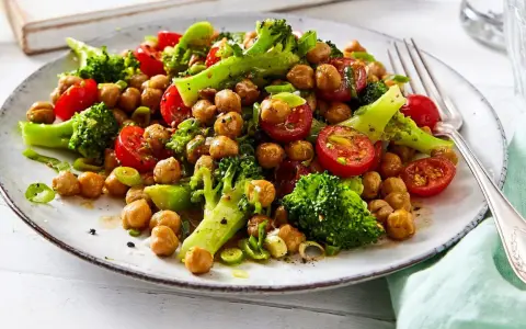 Frischer brokkoli kichererbsen salat mit Kirschtomaten und Frühlingszwiebeln auf einem Teller, appetitlich angerichtet.