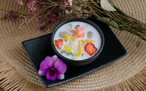 Schüssel mit cremigen asiatischen Nachspeisen, garniert mit Früchten und einer Orchidee.