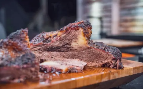 Saftiges Rind Brisket mit dunkler Kruste, auf einem Holzbrett serviert. Der Rauch steigt auf und verspricht ein zartes Geschmackserlebnis.
