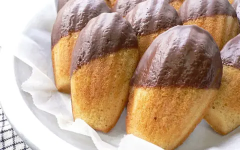 Eine Reihe von Madeleines, die zur Hälfte in Schokolade getaucht sind, warten darauf, gegessen zu werden.