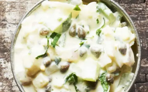 Cremiger Kartoffelsalat mit Kapern und frischen Kräutern, serviert in einer Metallschale auf rustikalem Holz.