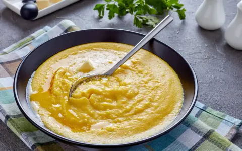 Eine Schüssel cremiger Polenta mit einem Stück Butter und einem Löffel. Was ist Polenta? Ein herzhaftes Maisgericht, das warm serviert wird.