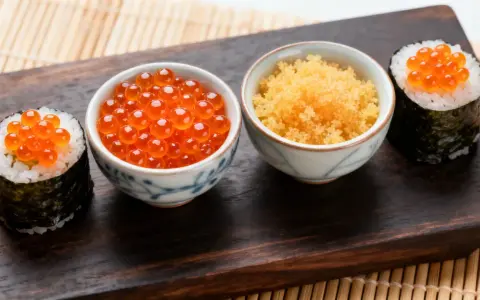 Zwei Sushi-Rollen mit Lachsrogen und eine Schale mit Masago, dem Rogen von Capelin-Fischen, daneben eine Schale mit Lachsrogen.