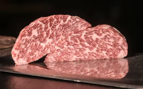 Zwei saftige Steaks vom Kobe Rind liegen auf einem metallischen Untergrund. Ihr auffälliges Marmormuster aus Fett und Fleisch verspricht ein einzigartiges Geschmackserlebnis.