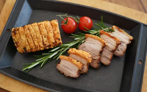 Knuspriger asiatischer Schweinebauch, in Scheiben geschnitten, mit Rosmarin und Kirschtomaten auf einer Gusseisenplatte serviert.