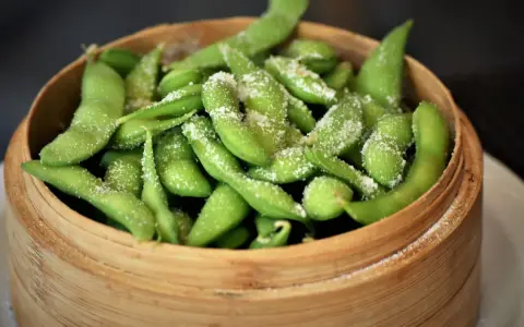 Frische Edamame-Schoten, leicht gesalzen, bereit zum rohen Essen. Ein gesunder Snack in einem Bambuskorb.