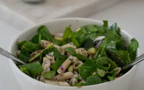 Ein frischer nudelsalat mit spargel, garniert mit Spinat und roten Zwiebeln, bereit zum Genießen.