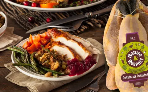 Ein festlich gedeckter Tisch mit einem Teller voller gebratenem Perlhuhn, dazu grüne Bohnen, Karotten und Cranberry-Sauce. Das unzubereitete Perlhuhn daneben zeigt das Label "Nature & Respect".