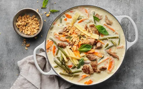 Herzhaftes Thai Curry mit Rindfleisch, zarten Möhren, grünen Bohnen und Maiskolben in cremiger Kokosmilch, garniert mit Erdnüssen und Basilikum.