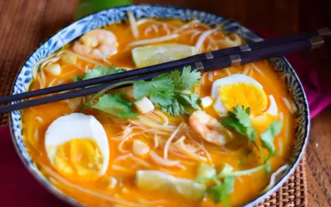 Eine Schüssel mit köstlicher Laksa Suppe, garniert mit Garnelen, Ei, Limette und Koriander.