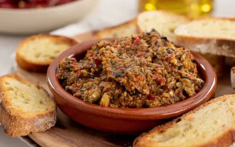 Herzhafte Tapenade deutsch in einer Tonschale, umgeben von geröstetem Brot. Ein Genuss für jeden Feinschmecker.