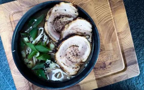 Schüssel mit Ramen-Nudeln, Brühe, Frühlingszwiebeln und drei Scheiben Chashu-Schweinebauch. Ein köstliches Chashu-Rezept!