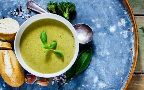 Grüne Detox-Suppe mit frischem Basilikum, dazu Baguettescheiben, Knoblauch und Brokkoli.