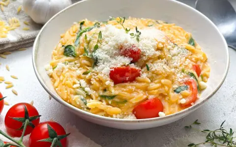 Cremiges One Pot Orzo mit Kirschtomaten, Spinat und Parmesan, garniert mit frischem Thymian.
