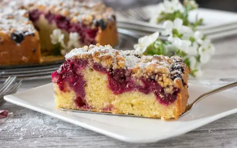 Ein saftiges Stück Streuselkuchen mit Marmelade und Puderzucker bestreut, bereit zum Genuss.