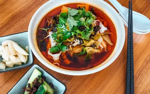 Eine Schüssel mit aromatischer taiwanischer Rindernudelsuppe, garniert mit frischem Koriander, daneben eingelegte Gurken und Rettich.