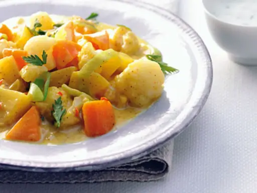 Ein Teller mit cremigem Curry-Eintopf, gefüllt mit Kartoffeln, Karotten und Lauch, garniert mit Petersilie.